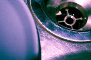 A person cleaning the black rubber splash guard of a kitchen garbage disposal with a brush and soapy water.