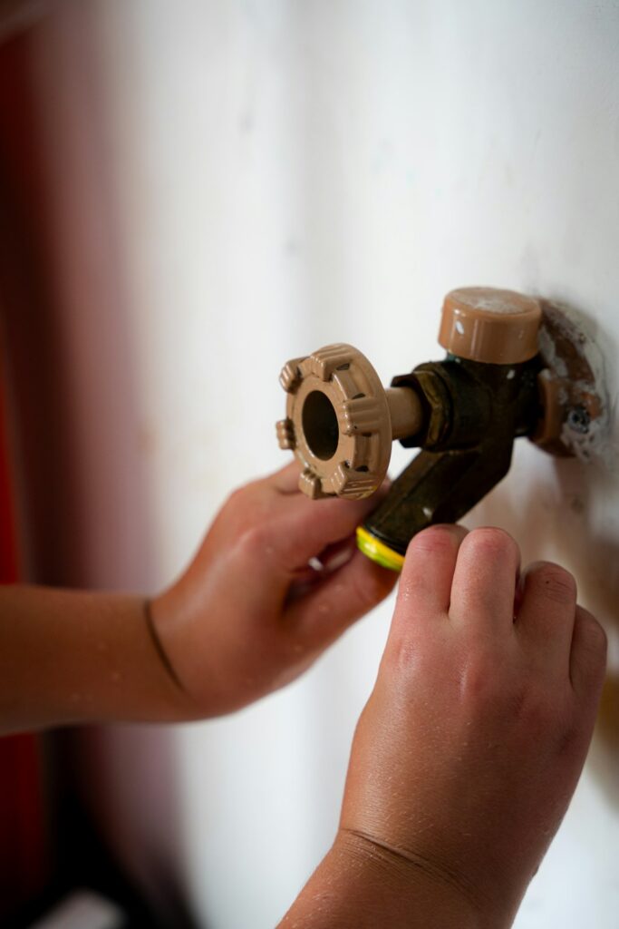 A pair of hands using pliers to adjust a toilet tank component with the lid off.