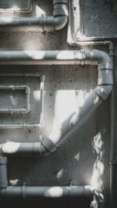 A person scratching a dull gray water pipe with a coin in a basement utility area.