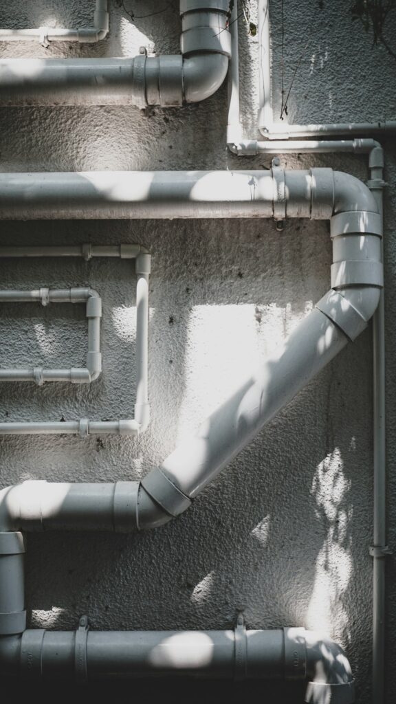 A person scratching a dull gray water pipe with a coin in a basement utility area.