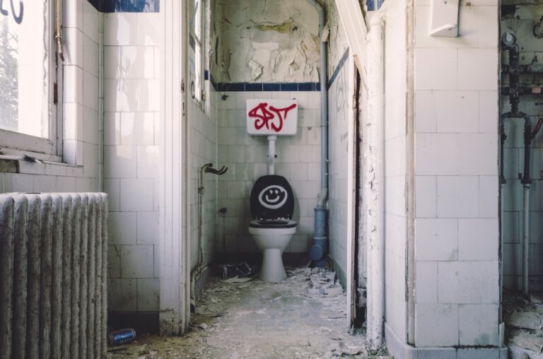 A person examining a toilet tank with the lid off and tools placed nearby on the bathroom floor.