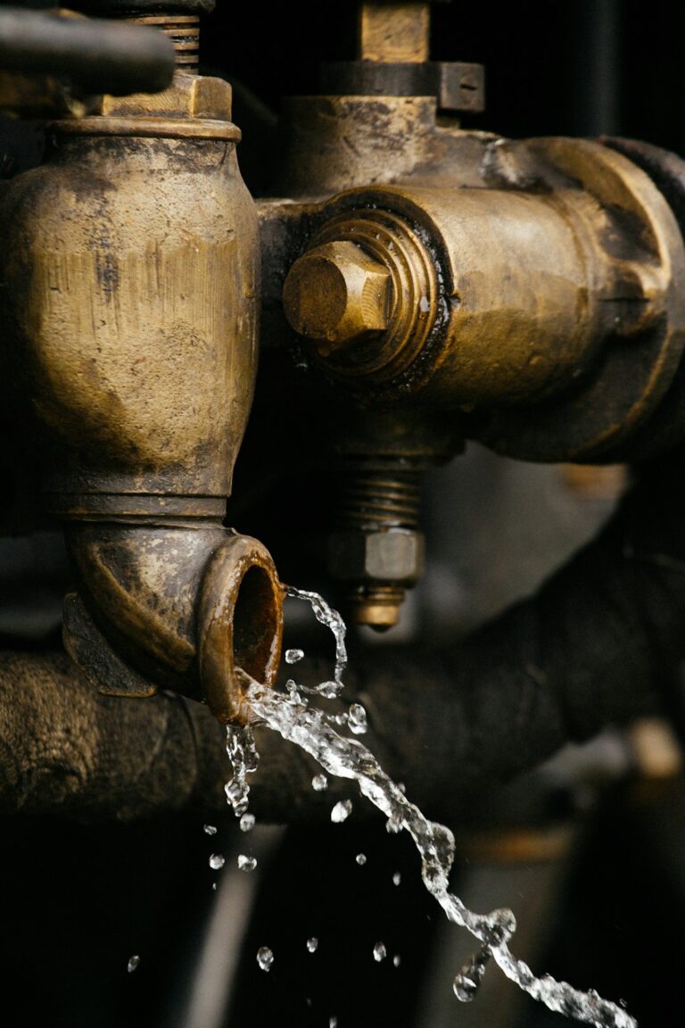 A person kneeling next to an exposed pipe under a kitchen sink, inspecting for moisture or leaks.