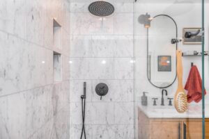 A person testing hot water flow in a household shower with tiled walls and a standard showerhead.