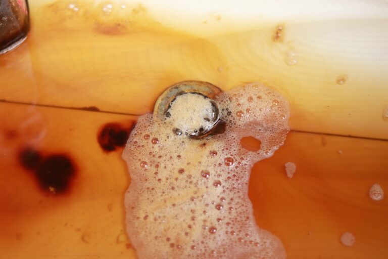 A person pouring cooled cooking grease into a metal can next to a kitchen sink.