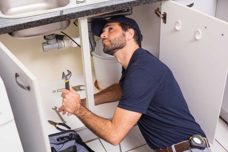 Homeowner checking a water heater while examining a nearby control panel and dry utility-room floor.