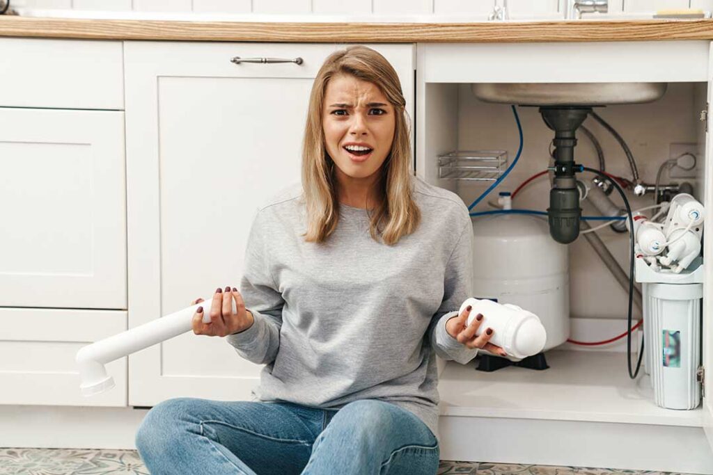 A person shines a flashlight beneath a sink while inspecting the P-trap for a dropped ring.